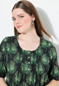 Černý top s motivem zeleného palmového listu, kulatým výstřihem, krátkými rukávy a detailním zapínáním na knoflíky vpředu. Hladká textura látky.