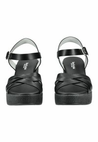 Sandales à plateforme en cuir noir avec des lanières croisées et des fermetures à boucle à la cheville, semelles texturées, vues de face sur un fond blanc.