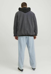 Giacca in polare grigia con cappuccio nero, caratterizzata da una vestibilità comoda. Abbinata a pantaloni larghi azzurri e sneaker nere con dettagli bianchi.