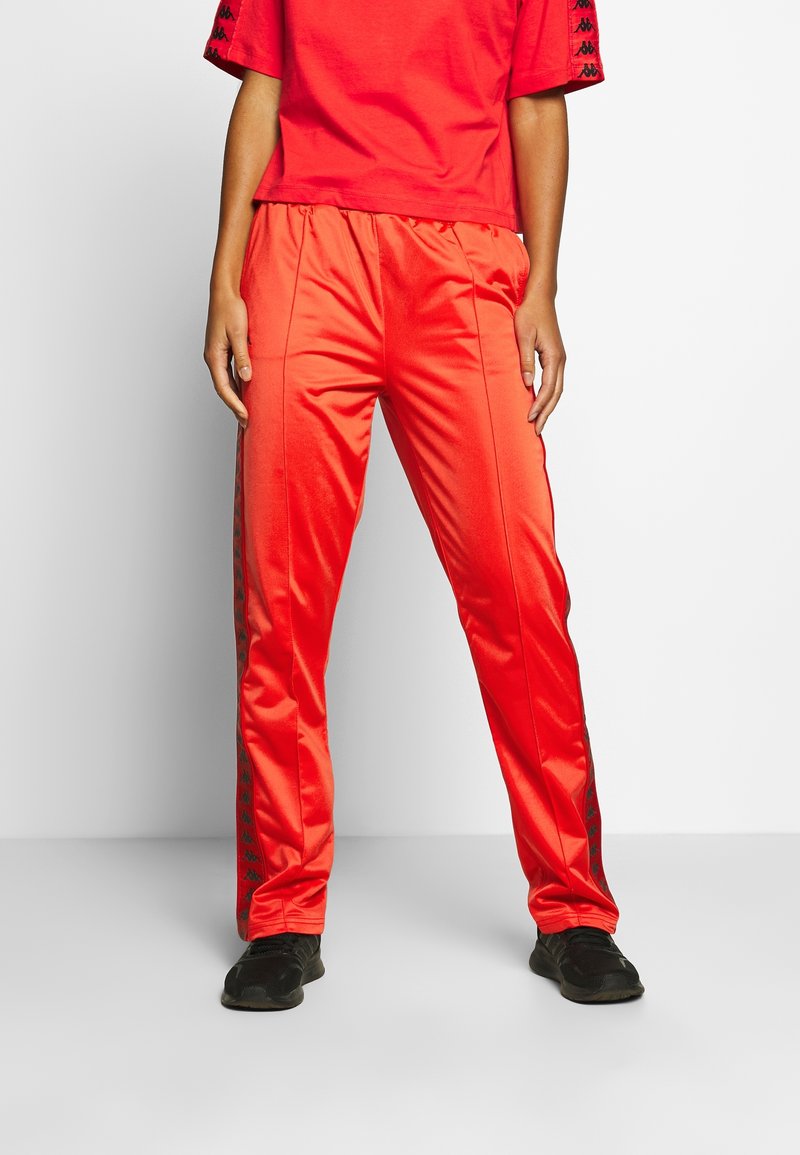 Røde satin træningsbukser med sorte sidelister med gentagne logomønstre. Har en elastisk talje og et lige ben-design.