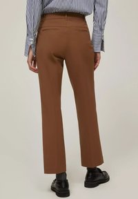 Pantaloni marroni tailored con design a gamba dritta, dotati di due tasche posteriori e un tessuto liscio e strutturato. Indossati con scarpe nere.