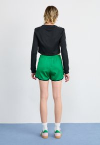 Black cropped jacket, green satin shorts, white socks, pink and green shoes, back view, clean lines, smooth textures, athletic style.
