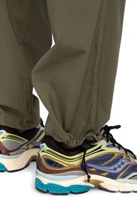 Olijfgroene, losvallende broek van textuurstof, met een elastische zoom. Multikleurige sportschoenen met mesh en patronenaccents.