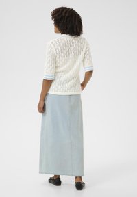 Vit, lätt stickad topp med håldesign, blå randiga ärmar, parat med en lång ljus denimkjol och svarta platta skor.