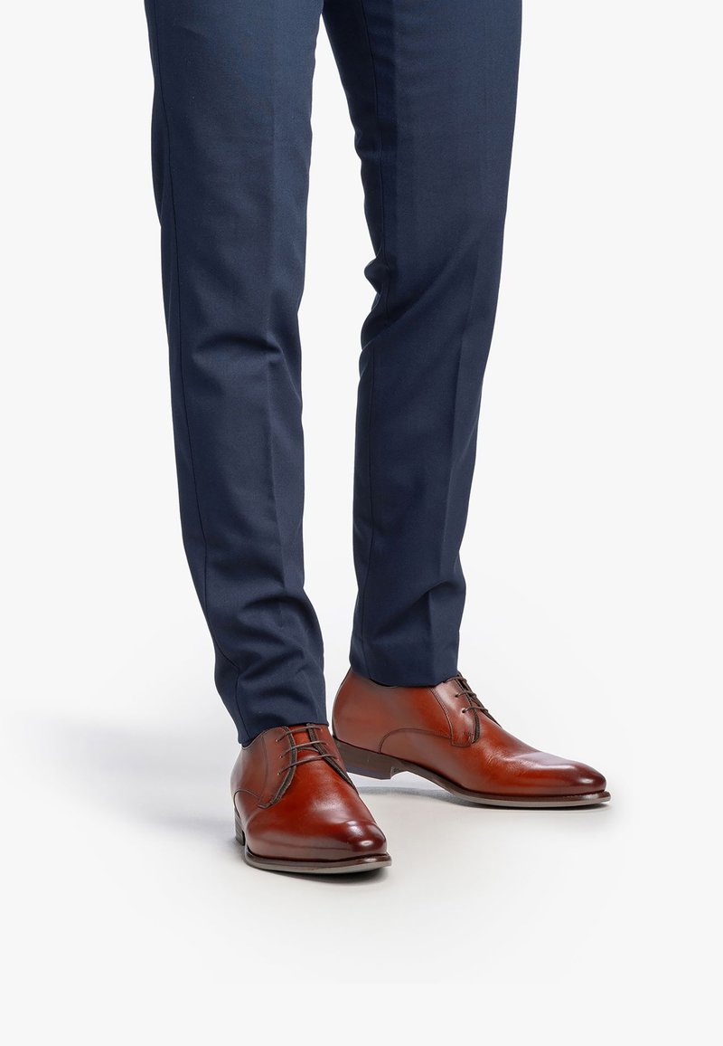 Glanzende bruine leren herenschoenen gedragen met donkerblauwe op maat gemaakte broek op een witte achtergrond.