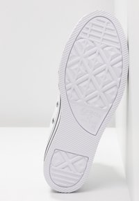 Semelle blanche de basket Converse All Star avec motif géométrique, inclinée contre une surface blanche montrant la taille 45.