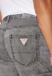 Šedé džíny z denimu s přiléhavým střihem, které mají trojúhelníkovou nášivku na zadní kapse a kontrastní prošívání.