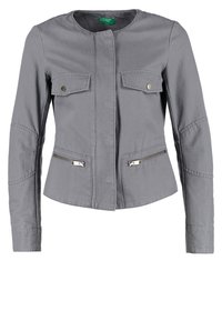 Chaqueta gris con escote redondo, dos bolsillos frontales con solapas y dos bolsillos laterales con cremallera. Presenta costuras detalladas y mangas largas.