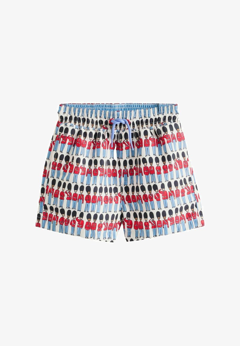 Children’s shorts with a repeating pattern of cartoon British guards in red uniforms and tall black hats on a white background.