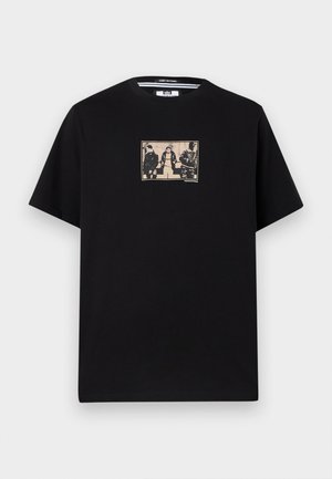 Črna majica s kratkimi rokavi z bež pravokotno grafiko na prsih, na kateri so trije ljudje v priložnostnih oblačilih sedeči in stoječi.