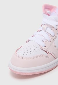 Nærbilde av en rosa og hvit sneakers med hvite snøringer og perforert tåparti på en ensfarget bakgrunn.