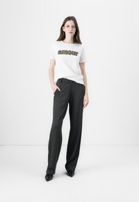 White t-shirt with "amour" text in black and gold, paired with high-waisted charcoal gray trousers. Model wearing black pointed shoes.