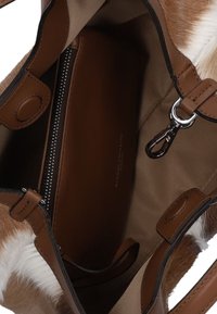 Borsa a mano in pelle marrone con un accento morbido e peloso. L'interno è in tessuto beige con una tasca con zip e una chiusura in metallo.