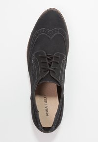 Chaussure oxford en suede noir à lacets avec des perforations décoratives et des coutures blanches, dotée d'un bout arrondi et d'une semelle intérieure rembourrée.