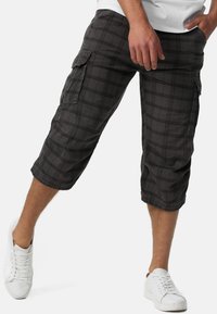 Shorts cargo à carreaux noirs avec poches latérales, longueur au genou et coupe décontractée, accompagnés de baskets blanches.