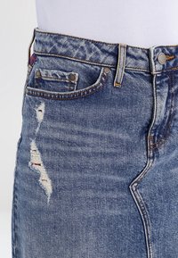 Siniset farkut haalistuneella viimeistelyllä, joissa on rispaantuneita kohtia, viisi taskua ja näkyvät saumat.