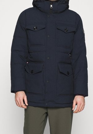 Giacca imbottita blu navy con cappuccio, dotata di quattro tasche frontali, bottoni a pressione e chiusura con zip. Texture opaca e senza motivi visibili.