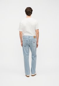 Ανοιχτό μπλε τζιν παντελόνι με ευθεία εφαρμογή, πέντε τσέπες και καφέ δερμάτινο ταμπελάκι στο πίσω μέρος. Συνδυασμένο με ένα απλό λευκό μπλουζάκι.