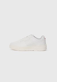 White sneaker with a textured upper, perforated detailing, a light grey mesh tongue, and a cream rubber sole. Features minimal branding on the side.