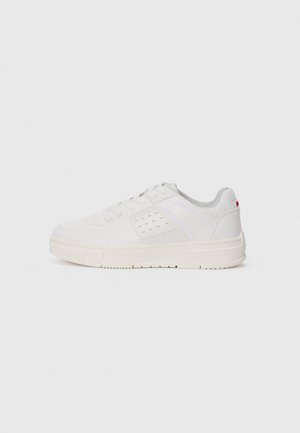 White sneaker with a textured upper, perforated detailing, a light grey mesh tongue, and a cream rubber sole. Features minimal branding on the side.