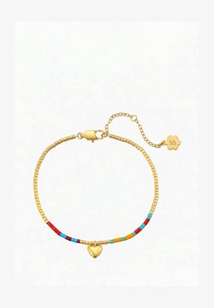 Pols met een delicate multicolour kralenarmband met een klein gouden harthanger, naast een wit mouwloos topje.
