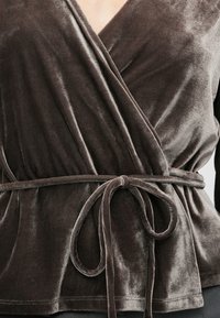 Top din catifea maro, cu un decolteu adânc în V, talie strânsă cu un cordon legat și o textură fină.