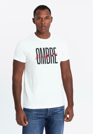 White cotton t-shirt featuring black and red text reading "OMBRE" in varied fonts. Round neckline and short sleeves, paired with blue jeans.