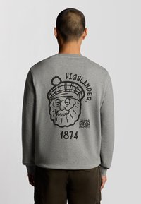 Felpa grigia con collo tondo e maniche lunghe. Presenta una grafica sul retro di un personaggio con barba che indossa un cappello, con "HIGHLANDER" sopra e "1874" sotto.