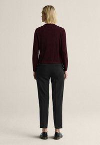 Vinröd figursydd tröja med långa ärmar kombinerad med svarta skräddarsydda byxor. Outfiten har en minimalistisk design och slät tygstruktur.