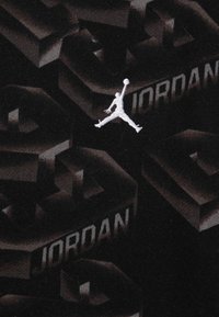 Il tessuto nero presenta un design testurizzato prominente con lettering in rilievo "JORDAN" e un logo Jumpman ricamato bianco.