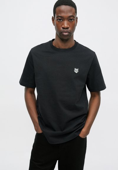Tricou din bumbac negru cu guler rotund și mâneci scurte, având un mic emblema gri cu un lup pe partea stângă a pieptului.