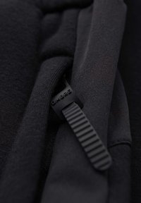Gros plan sur un tissu noir avec une sangle en caoutchouc côtelée étiquetée « OMBRE » passée à travers une boucle.