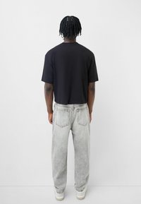 Maglietta nera a maniche corte e taglio cropped, abbinata a jeans grigi chiari a vita alta. L'outfit presenta una vestibilità rilassata e dettagli minimi.