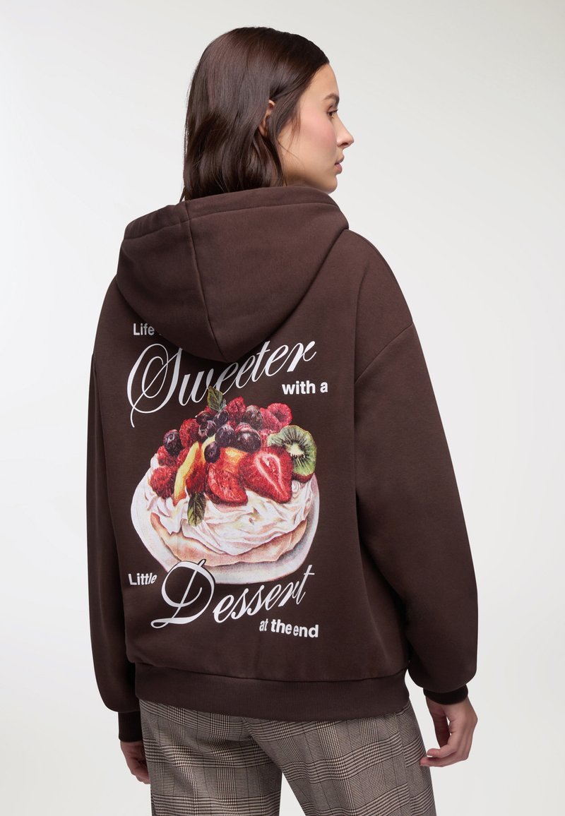 Felpa con cappuccio marrone con una grafica colorata di un dessert sul retro e testo bianco. Vestibilità comoda e tessuto morbido. Polsini rigati alle maniche.