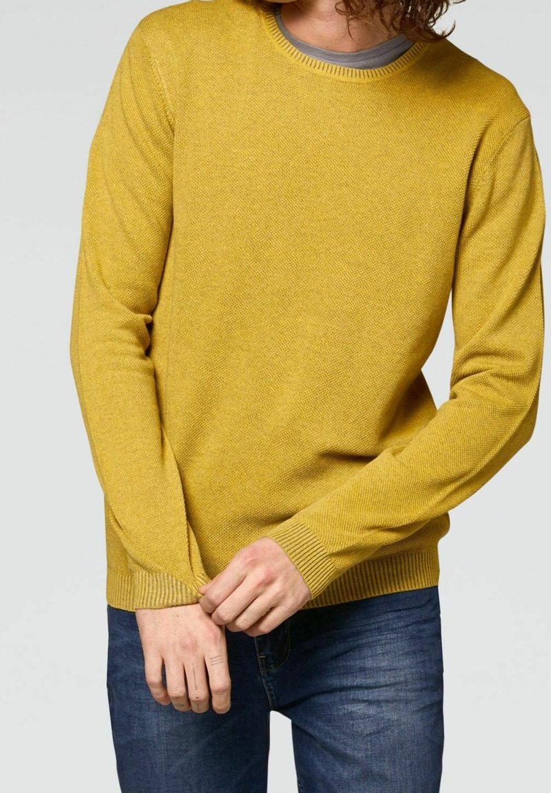 Geel gebreid truitje met een ronde hals en ribgebreide mouwen. Gedragen met blauwe jeans, met een gestructureerde stof en een licht getailleerd ontwerp.