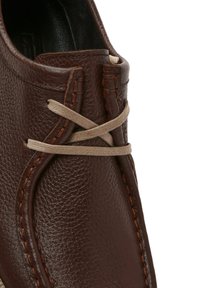 Scarpa in pelle marrone con superficie texturizzata, cuciture sovrapposte e un lace di colore chiaro intrecciato nella parte superiore per un fissaggio sicuro.