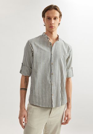 Chemise rayée en tissu léger, avec des rayures verticales bleues et blanches, un col mandarin et des manches retroussées. Des boutons marron ornent le devant.