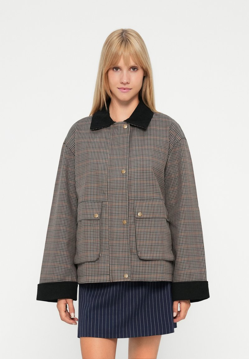 Giacca a quadri marrone con ampie tasche, bottoni dorati e colletto in velluto a coste nero. Presenta maniche oversize e una vestibilità rilassata.
