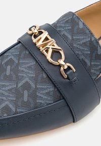 Mocassin pour homme bleu marine à motif, avec un détail de chaîne en métal doré portant le logo MK sur la bride avant.