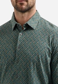 Groene blouse met een diamantpatroon, met een button-down kraag en zwarte knopen, gemaakt van een gestructureerde stof.