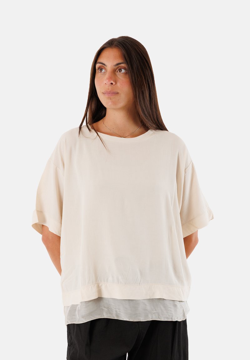 Top oversized beige chiaro con maniche corte, realizzato in un tessuto morbido e liscio. Presenta un design con orlo a strati e una vestibilità rilassata.