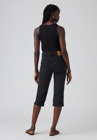 Svarte avkortede bukser med en tettsittende design, fem lommer og et lærmerke på baksiden av livet. Har diskret søm og rett snitt.