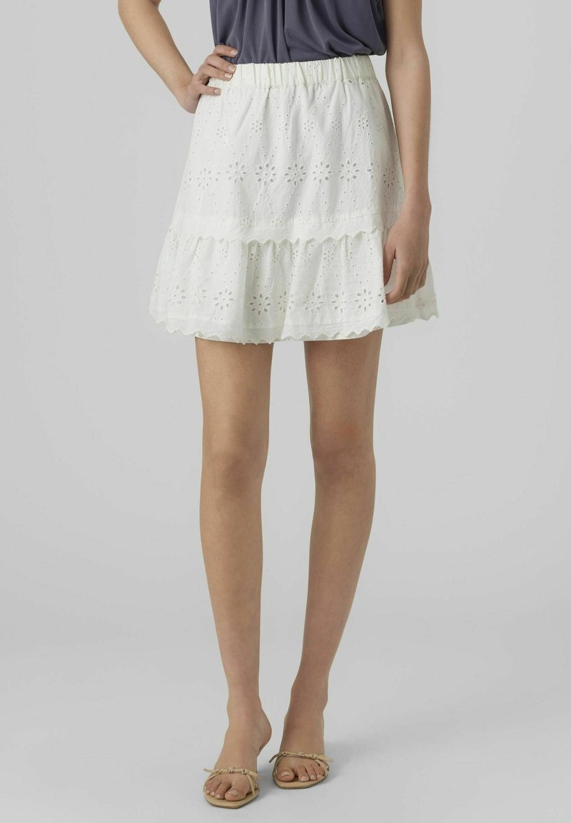 Vit ögonstickad kjol med en utställd silhuett, med en volangkant, elastisk midjeband och blommönstrade utskärningar genom hela kjolen.