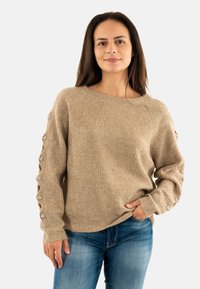 Maglione beige con texture a coste, dotato di una scollatura ampia e maniche lunghe con bottoni decorativi lungo i lati.