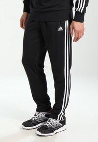 Czarne spodenki sportowe z trzema białymi paskami po bokach, wykonane z gładkiego, lekkiego materiału, z tapered fit i elastyczną talią.