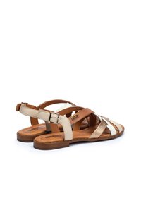 Bruine, beige en witte leren sandaal met kruislings straps, verstelbare enkelgesp en een platte bruine zool met stikseldetails.