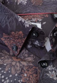 Korte mouw shirt met een donker bloemenpatroon in bruin- en grijstinten, voorzien van zwarte knopen en een kraagdetail.