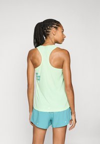 Top atlético en verde claro con diseño de tirantes en la espalda y texto impreso en la parte posterior. Combinado con pantalones cortos en azul verdoso; tiene un tejido ligero y transpirable.
