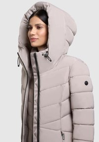 Padded jacket v svetlosivej farbe, s veľkým vysokým golierom, čiernym zipsom a nastaviteľnými šnúrkami. Výrazný prešívaný vzor na tele.