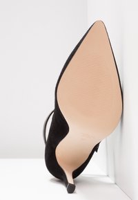 Stiletto à talon aiguille noir en daim, avec un bout pointu, doté d'un talon fin et d'une semelle beige lisse avec une texture antidérapante et les détails du fabricant.